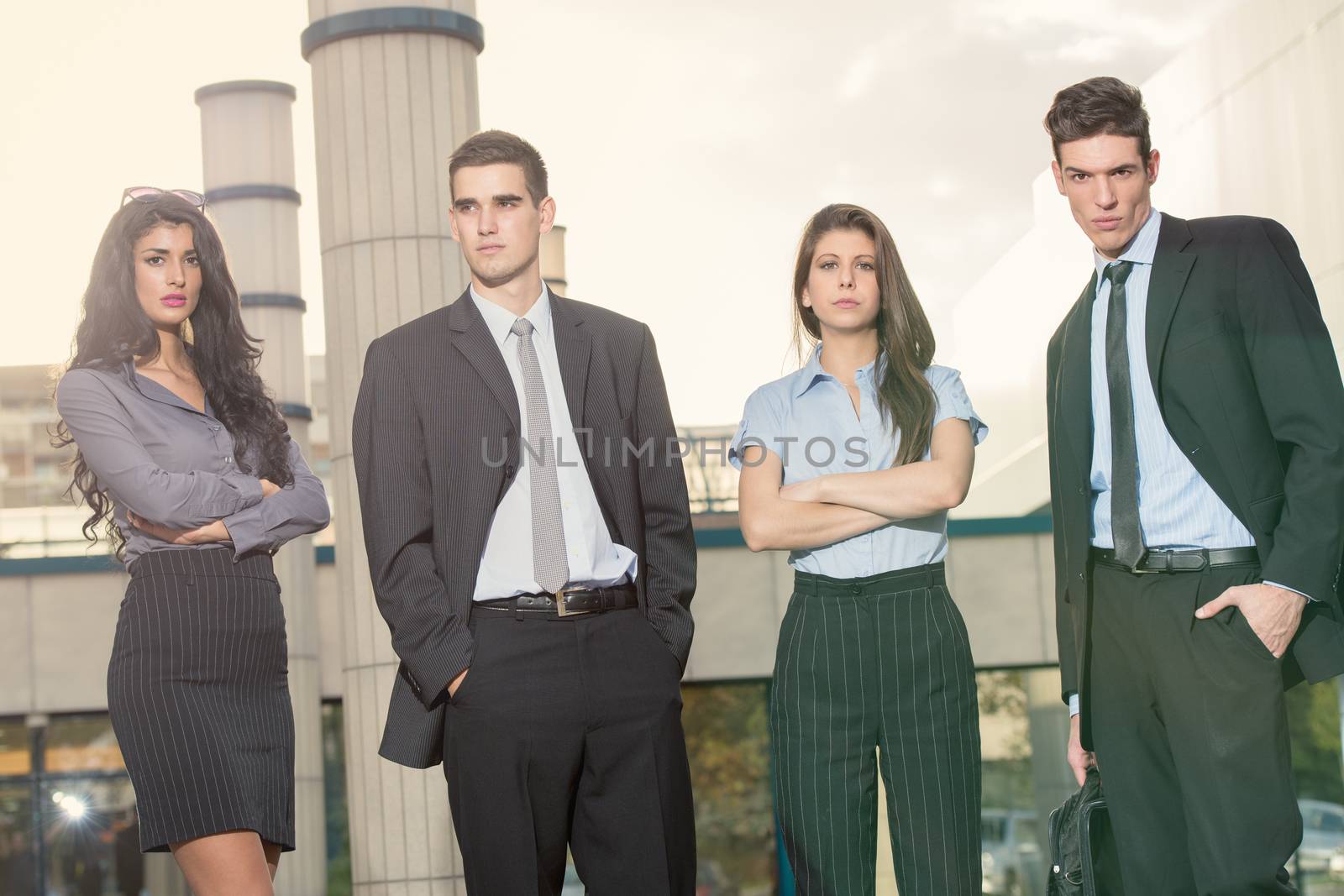 Group of young successful business people standing in front of office building dressed in elegant suits.