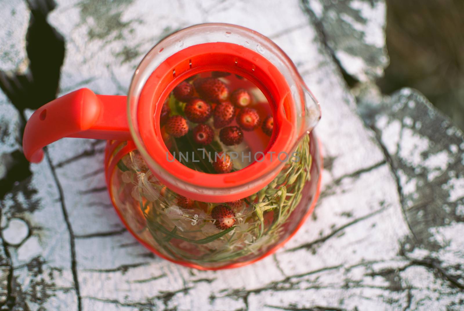 teapot of fruit tea with herbs and berry on the white tree stump. top view