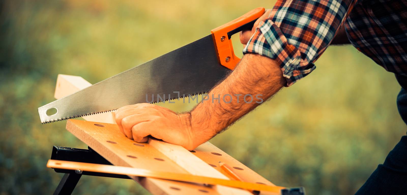 Carpenter sawing a wooden square with a wood saw outdoor