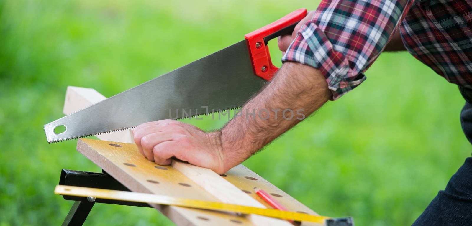 Carpenter sawing a wooden square with a wood saw outdoor