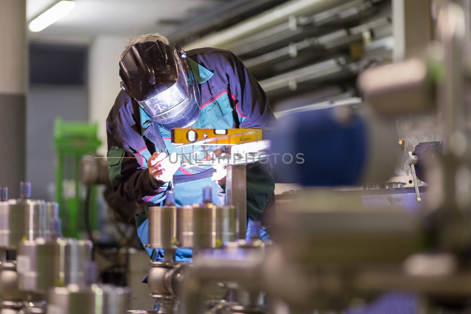 Industrial worker with protective mask welding inox elements in steel structures manufacture workshop.