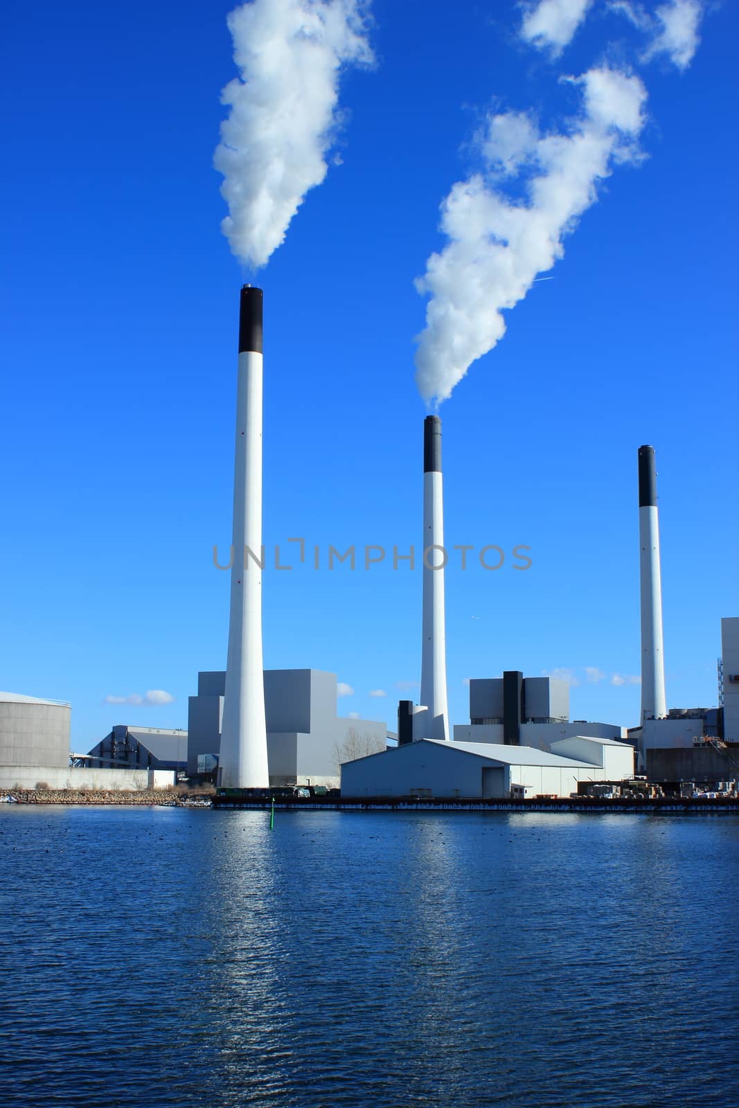 Factory chimneys at energy plant with blue sky and lake by HoleInTheBox