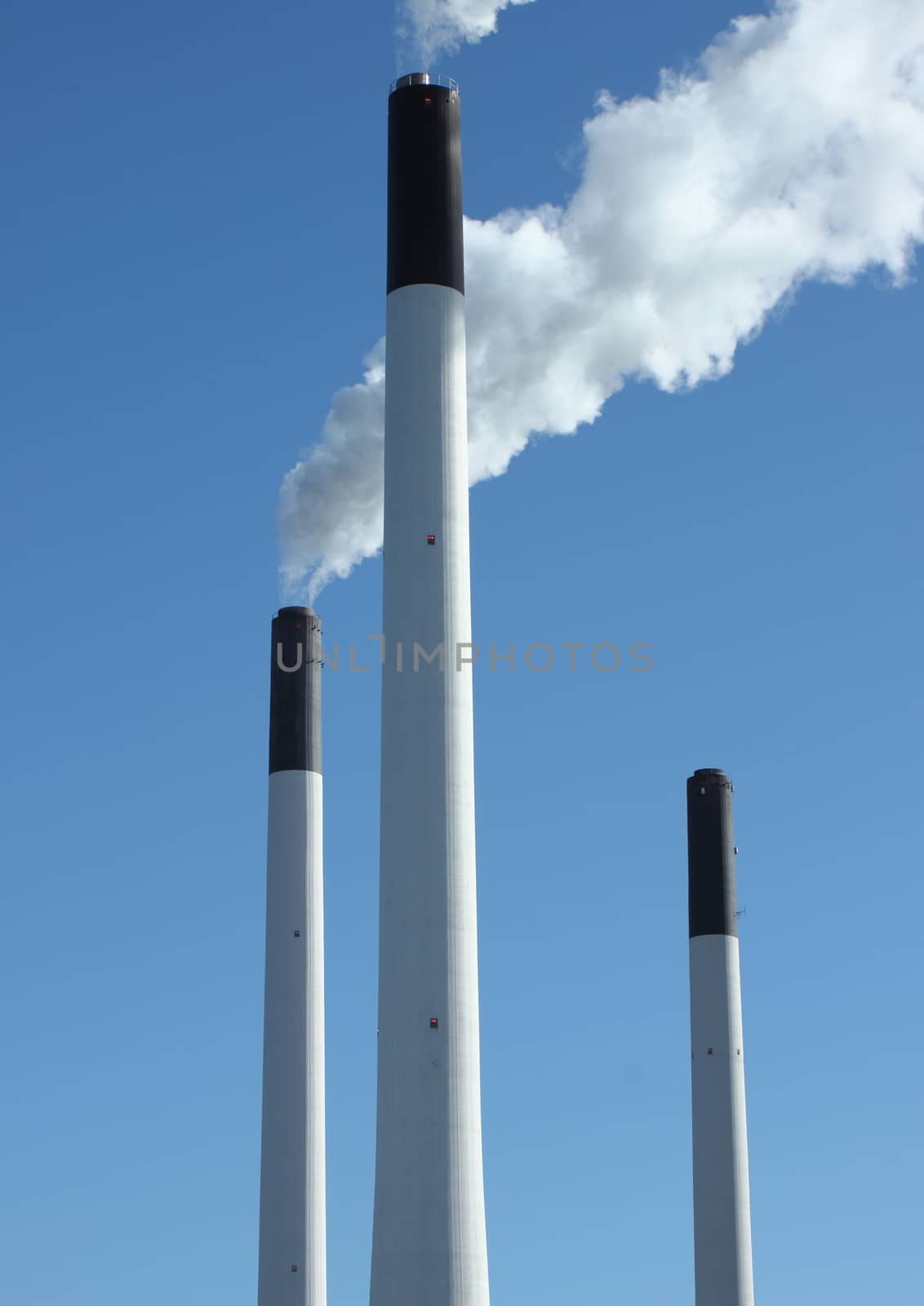 Factory chimneys at energy plant with blue sky and lake by HoleInTheBox