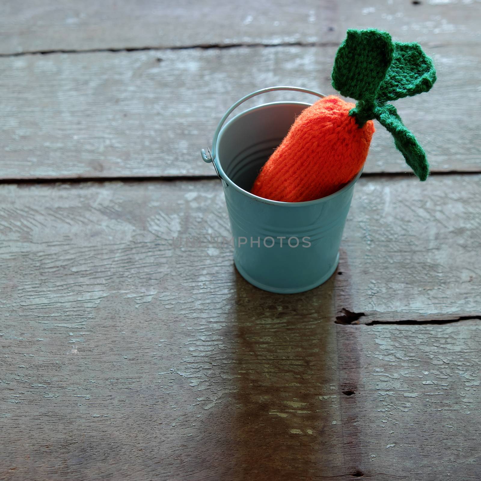 Knitted carrot vegetable on wood background, funny diy by knit from yarn, orange carot with green leaf