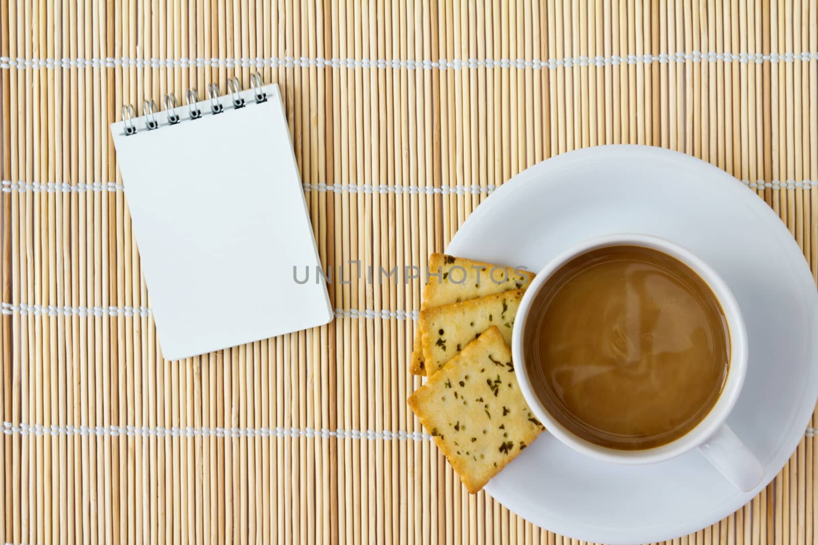 White cup of hot coffee and white sketch book on a mat 