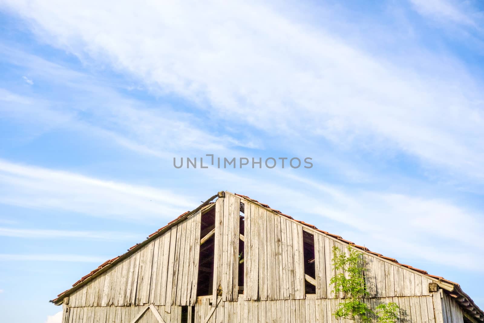 Roof of an old broken barn, blue sky with clouds
