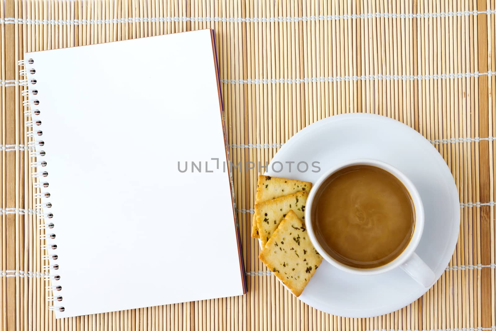 White cup of hot coffee and white sketch book on a mat 