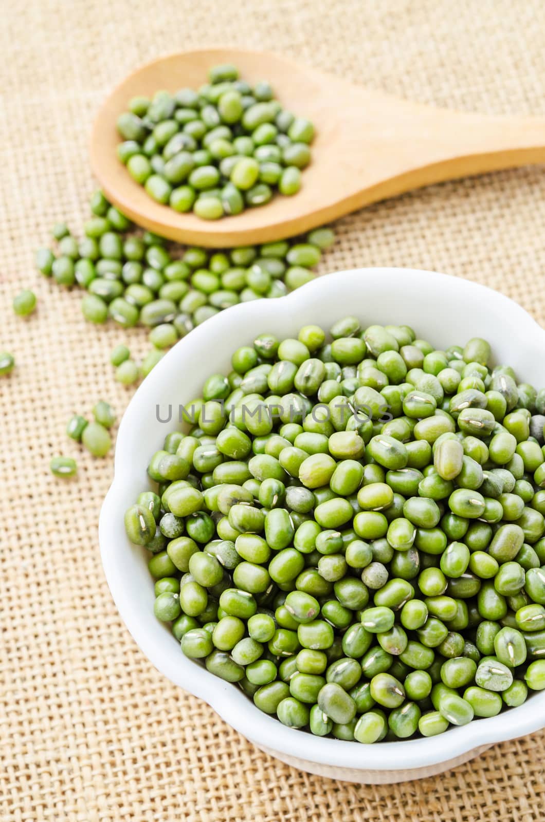 Mung beans seeds in white cup on sack background.