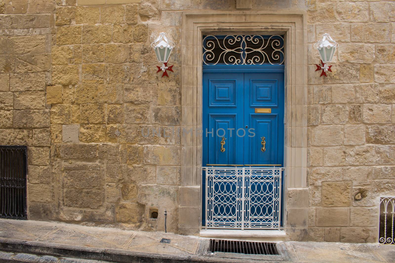 Bright blue door - entrance to an old stone house. Decorative lanterns with the maltese cross base. Seglea, island Malta.