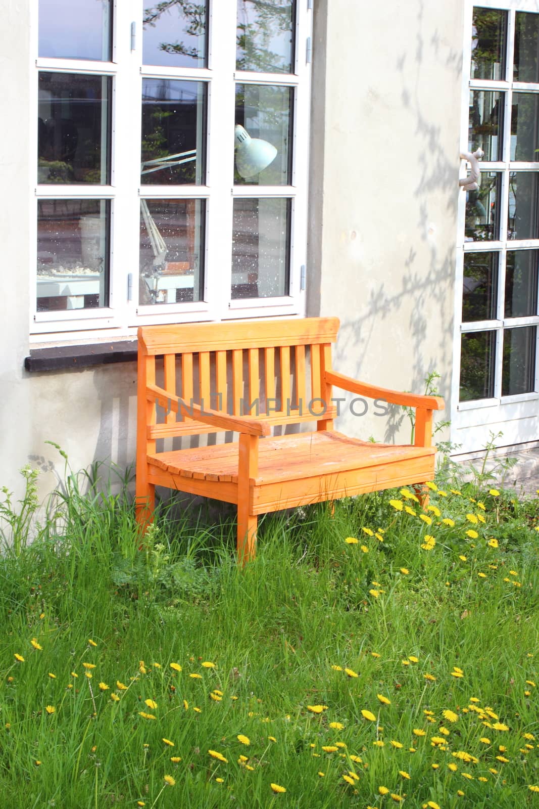 Orange bench on grass with window and lamp in background