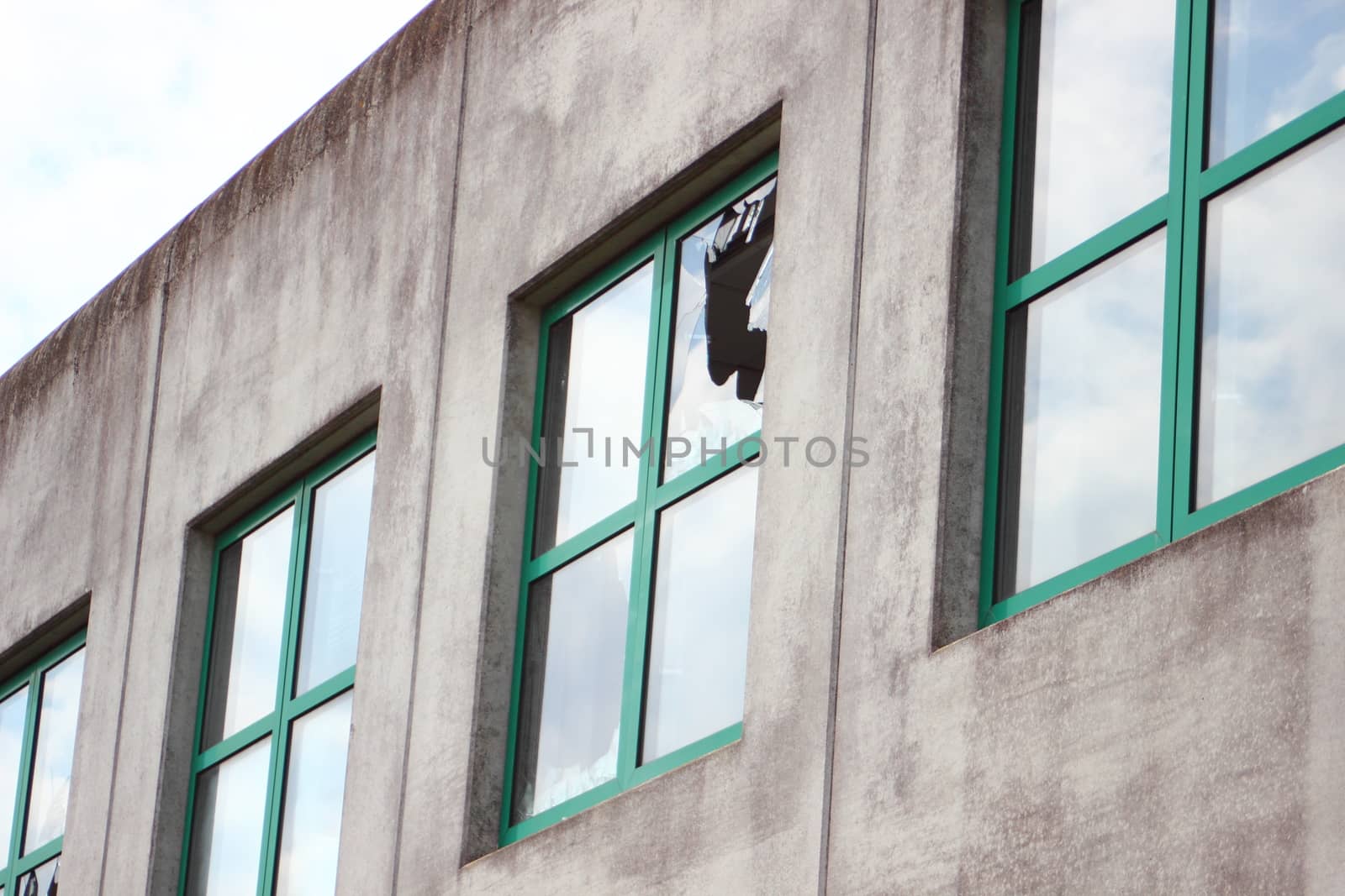 Broken glass in window with green frame at  factory by HoleInTheBox