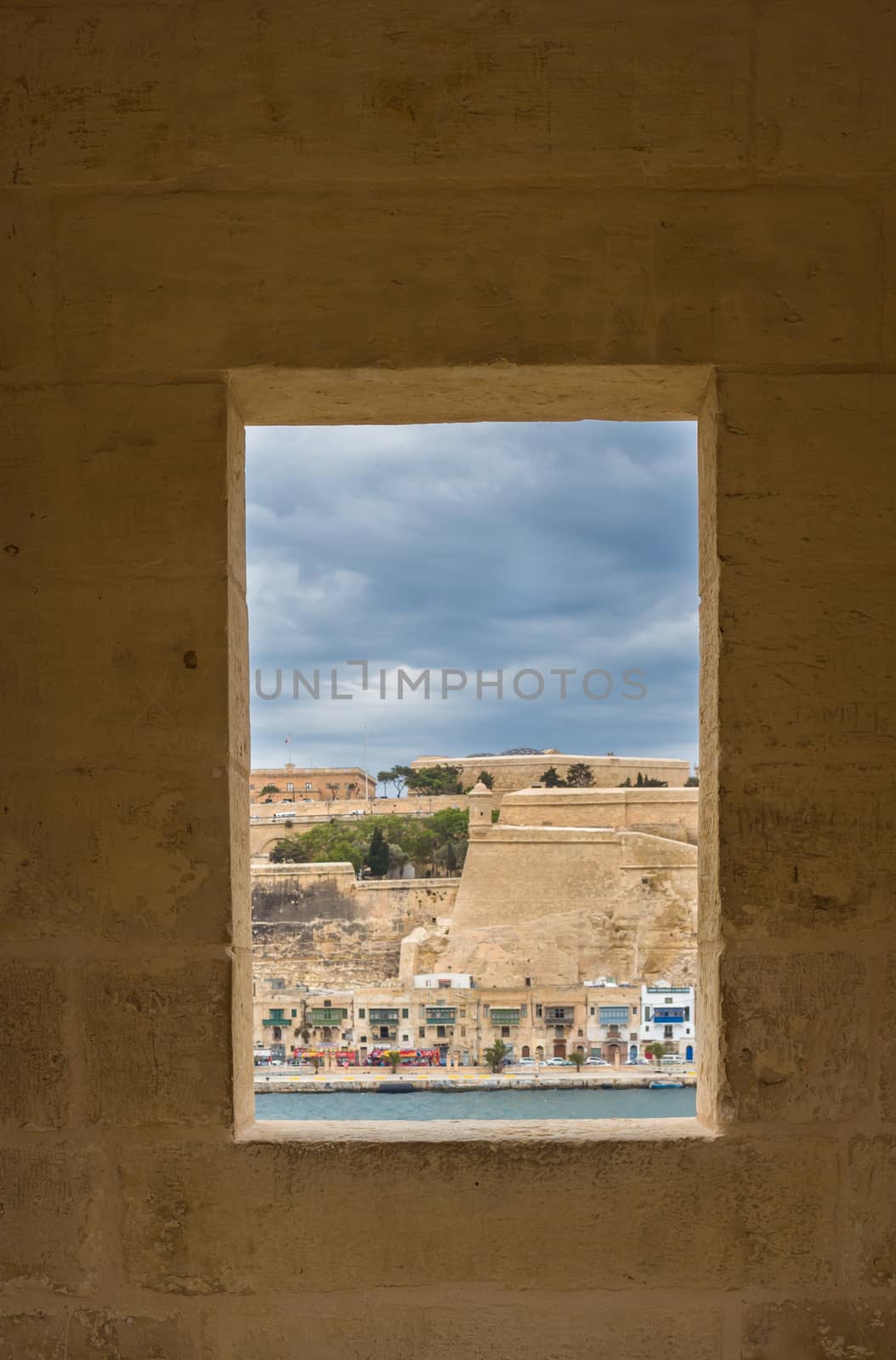 Window in the fortification tower in Gardjola Gardens in the city Senglea, island Malta. View on fortification of the capital Valletta. Cloudy sky.