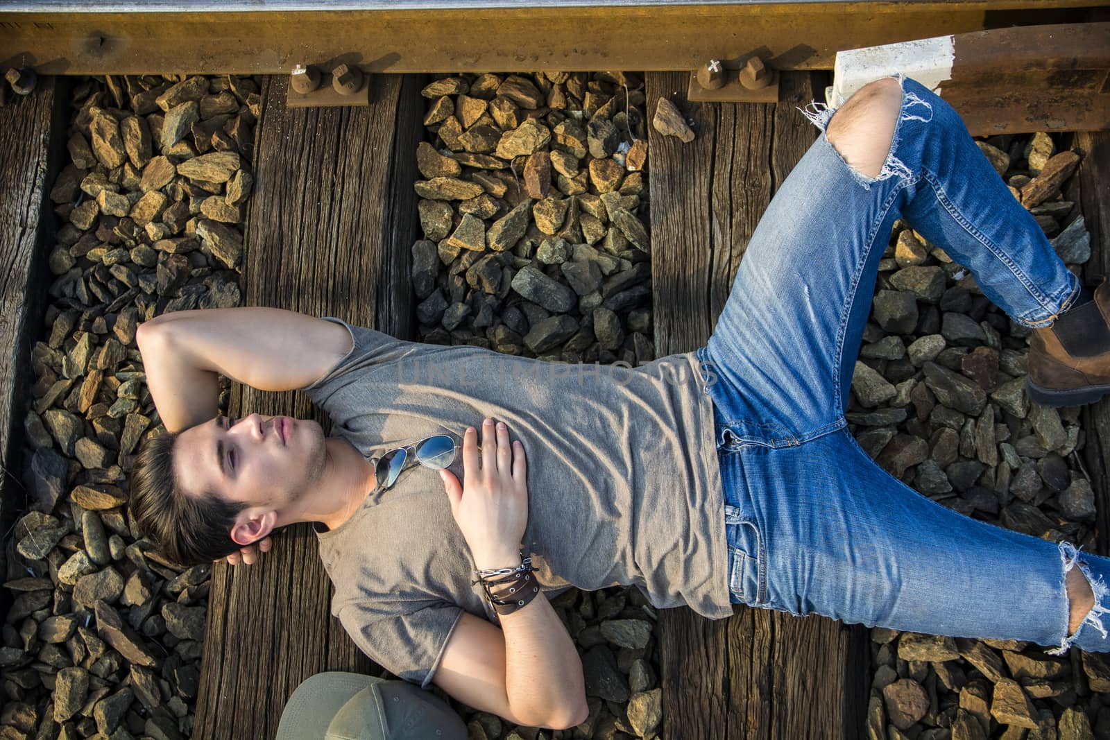 Attractive young man lying on railroad, wearing grey t-shirt and jeans, looking to a side