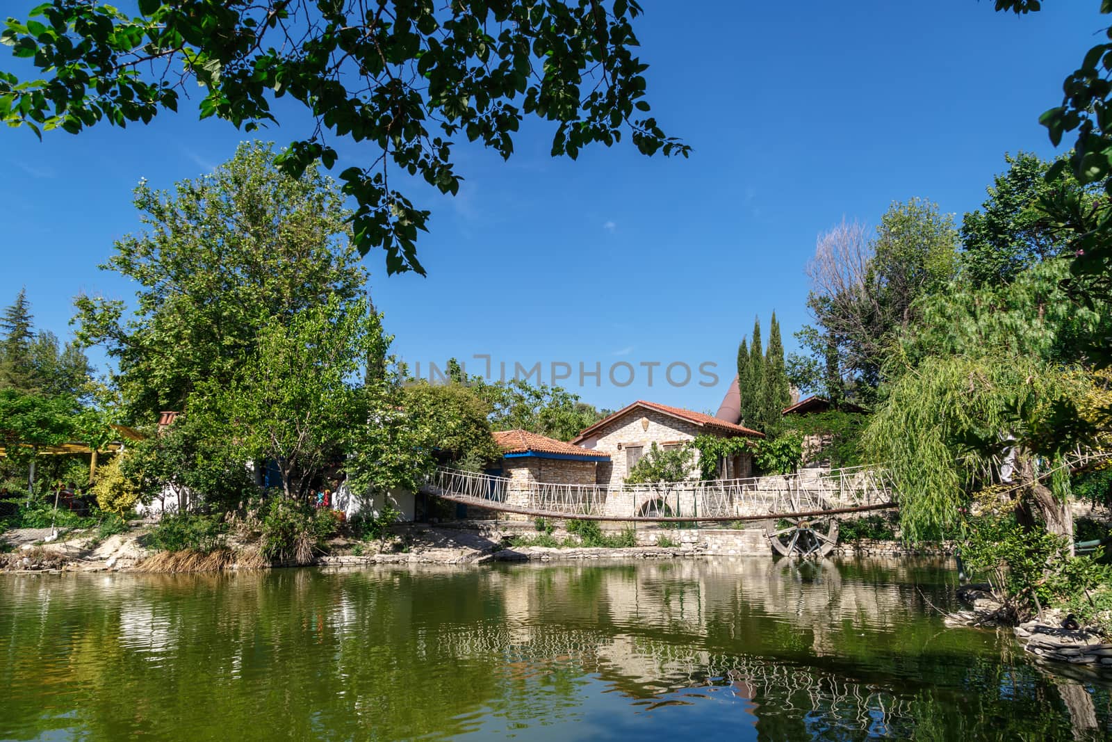 Landscape view of natural park with lake, trees and wooden arbour on bright blue sky background.