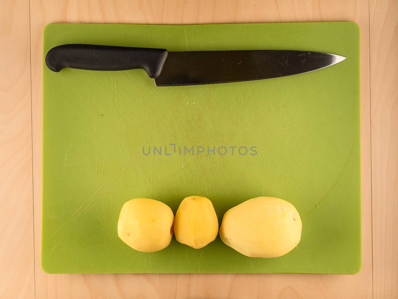 Several three peeled potatoes on green plastic board with knife, simple food preparation illustration, vegetarian dieting, top view still life with center composition and copy space
