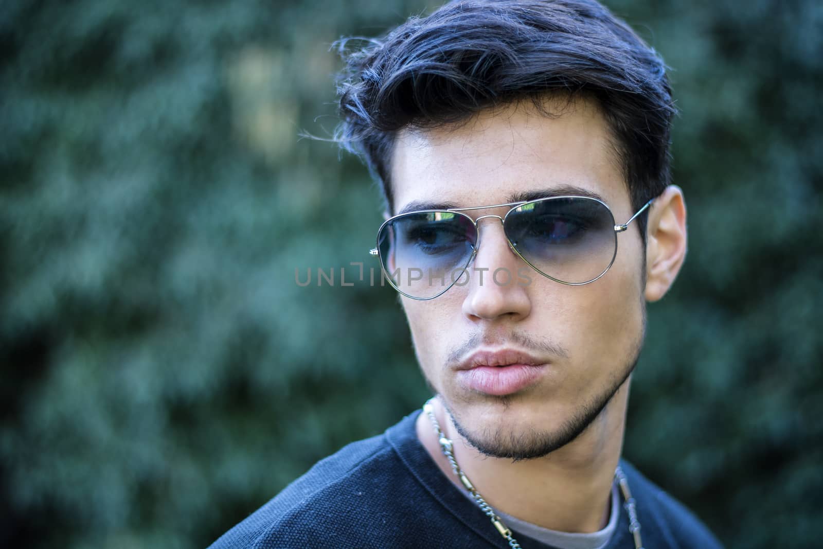 Headshot of handsome young man in city street, looking to a side, wearing sunglasses