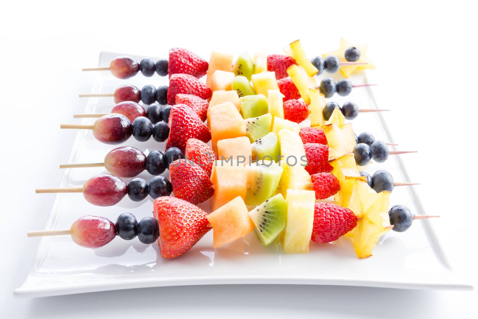 Serving of colorful fresh tropical fruit kebabs on a modern rectangular white plate viewed low angle with receding perspective on white