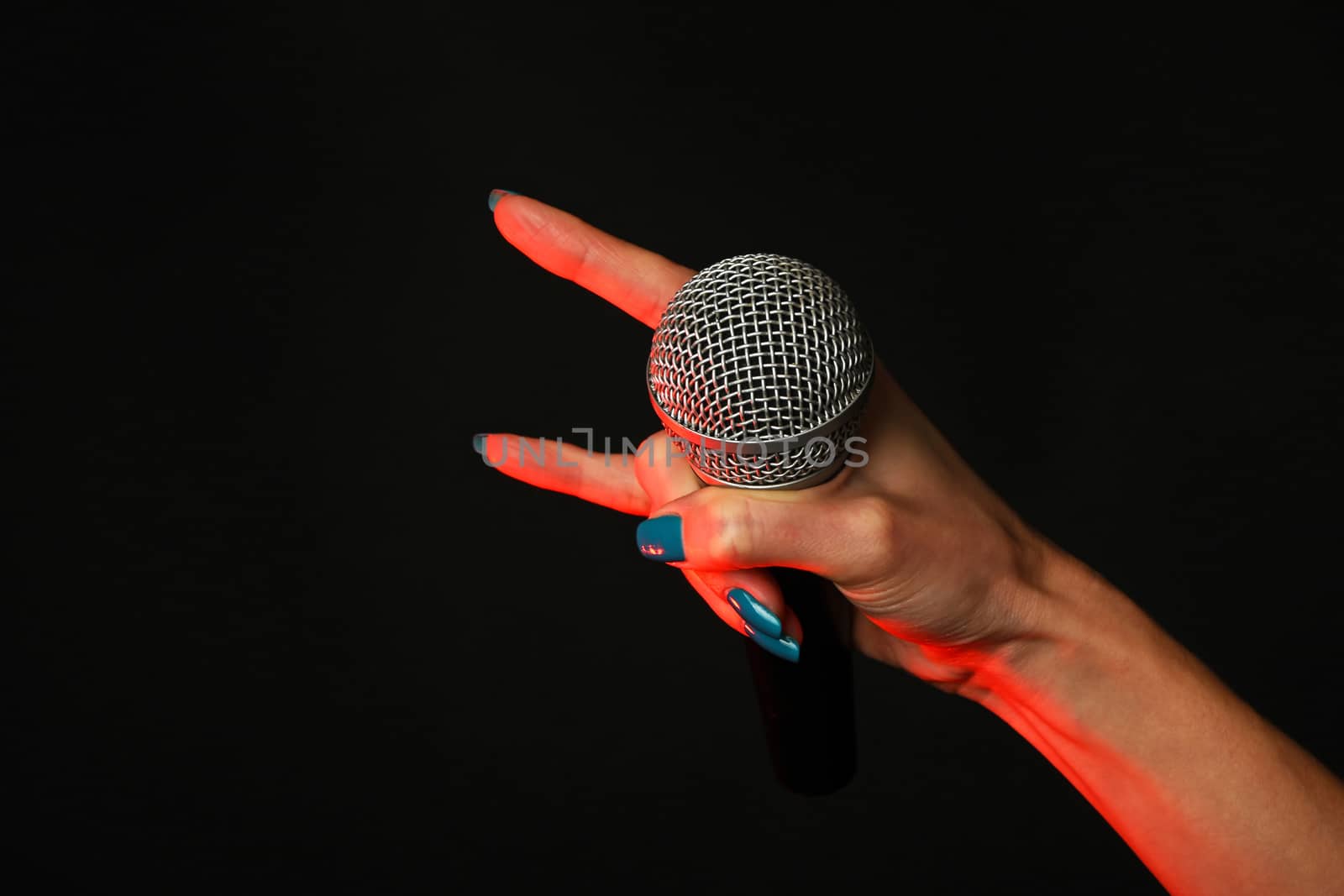 Woman hand with microphone with devil horns rock metal sign highlighted with red gun projector isolated on black background