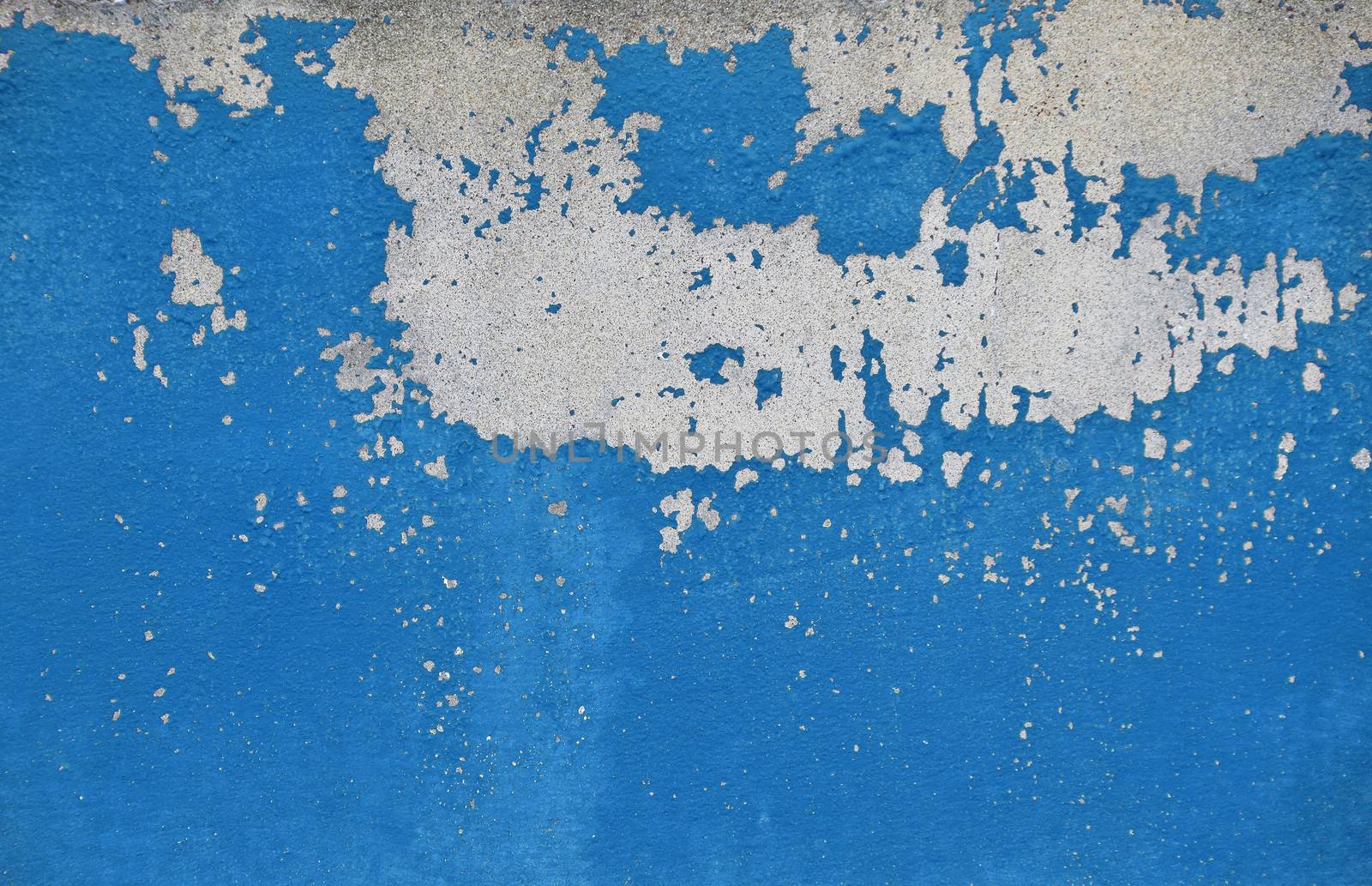 Flakes of old vintage grungy bright vivid blue paint on grey concrete wall