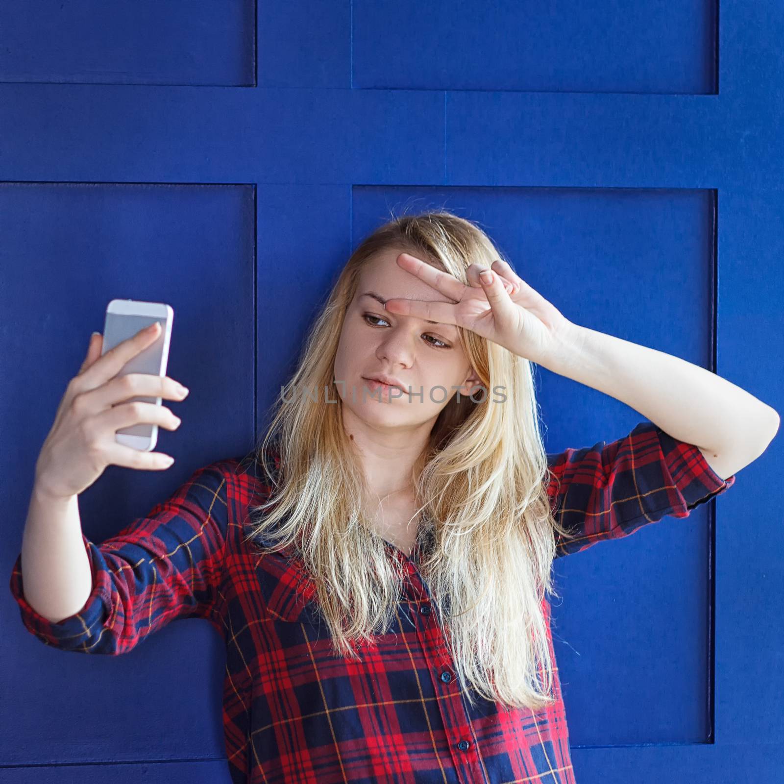 Portrait of a young attractive woman making selfie photo on smartphone near a blue background