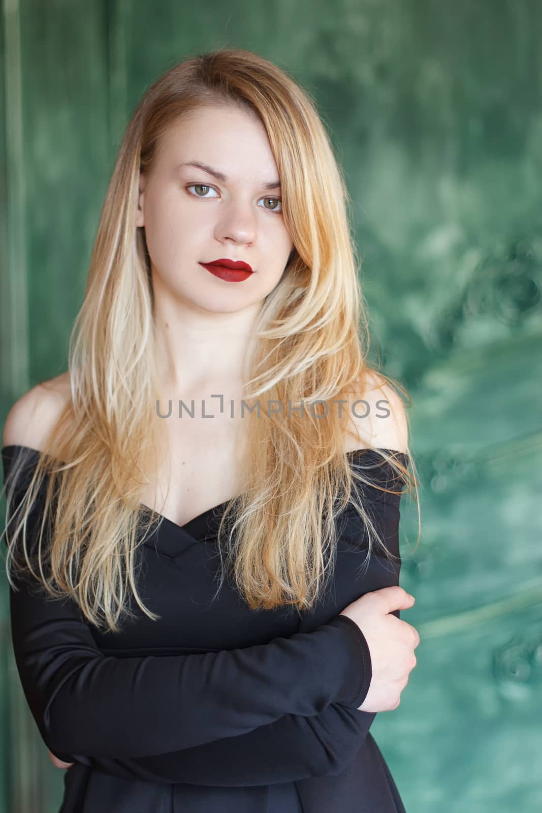Young stunning attractive girl posing in black dress. Portrait of girl standing against wall indoors