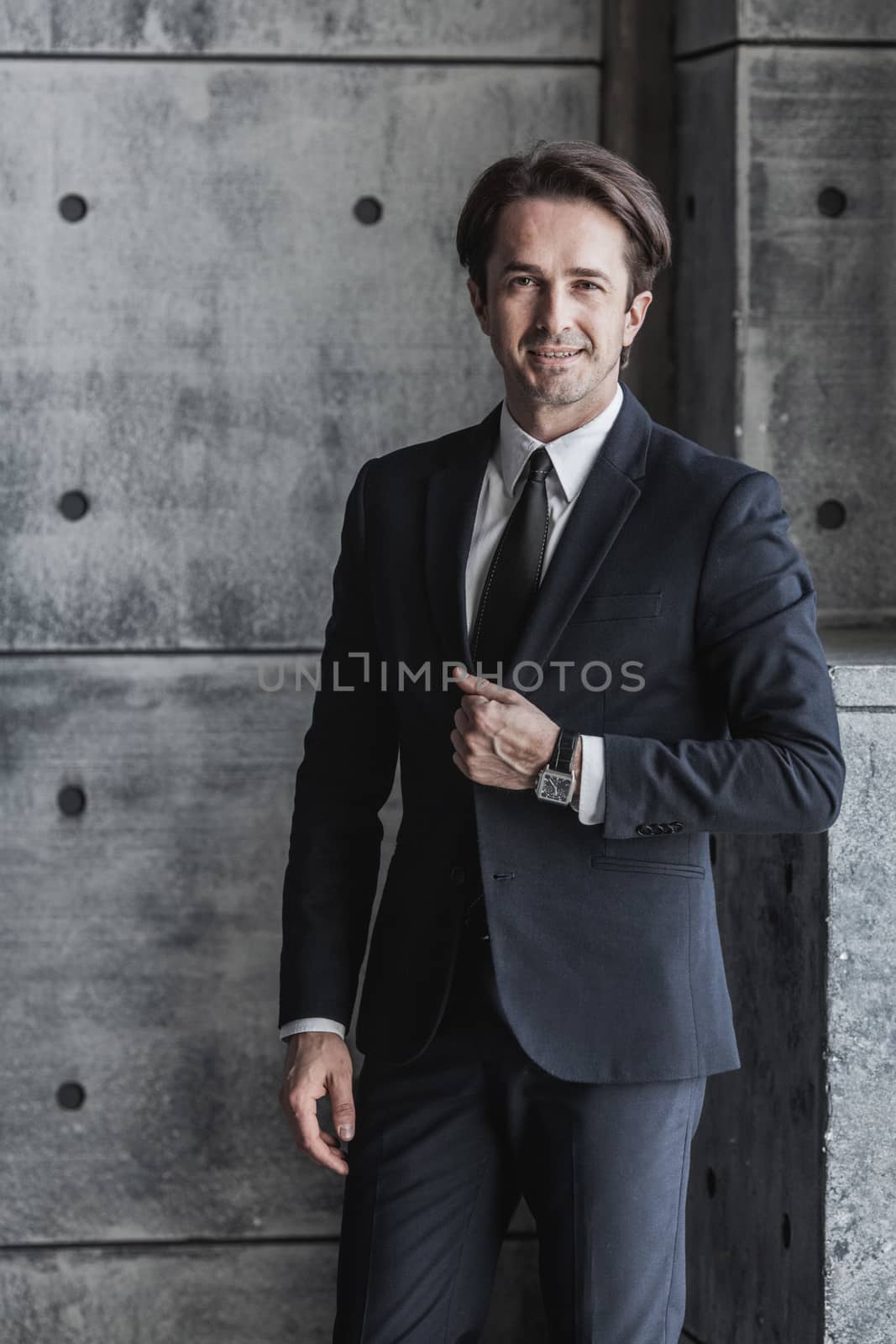 Portrait of smiling businessman in suit over concrete wall background