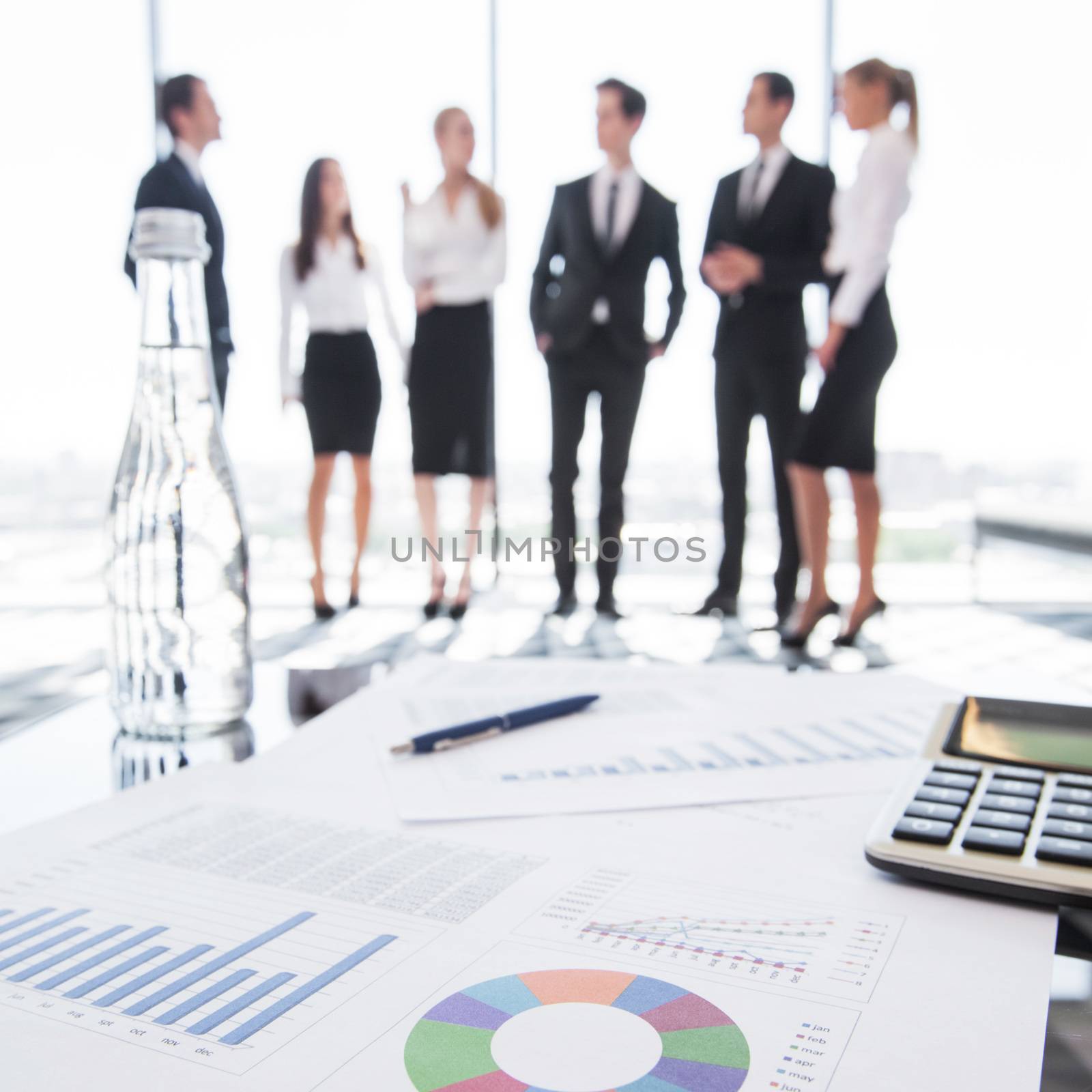 Close-up of financial reports and calculator, business people team standing in the background