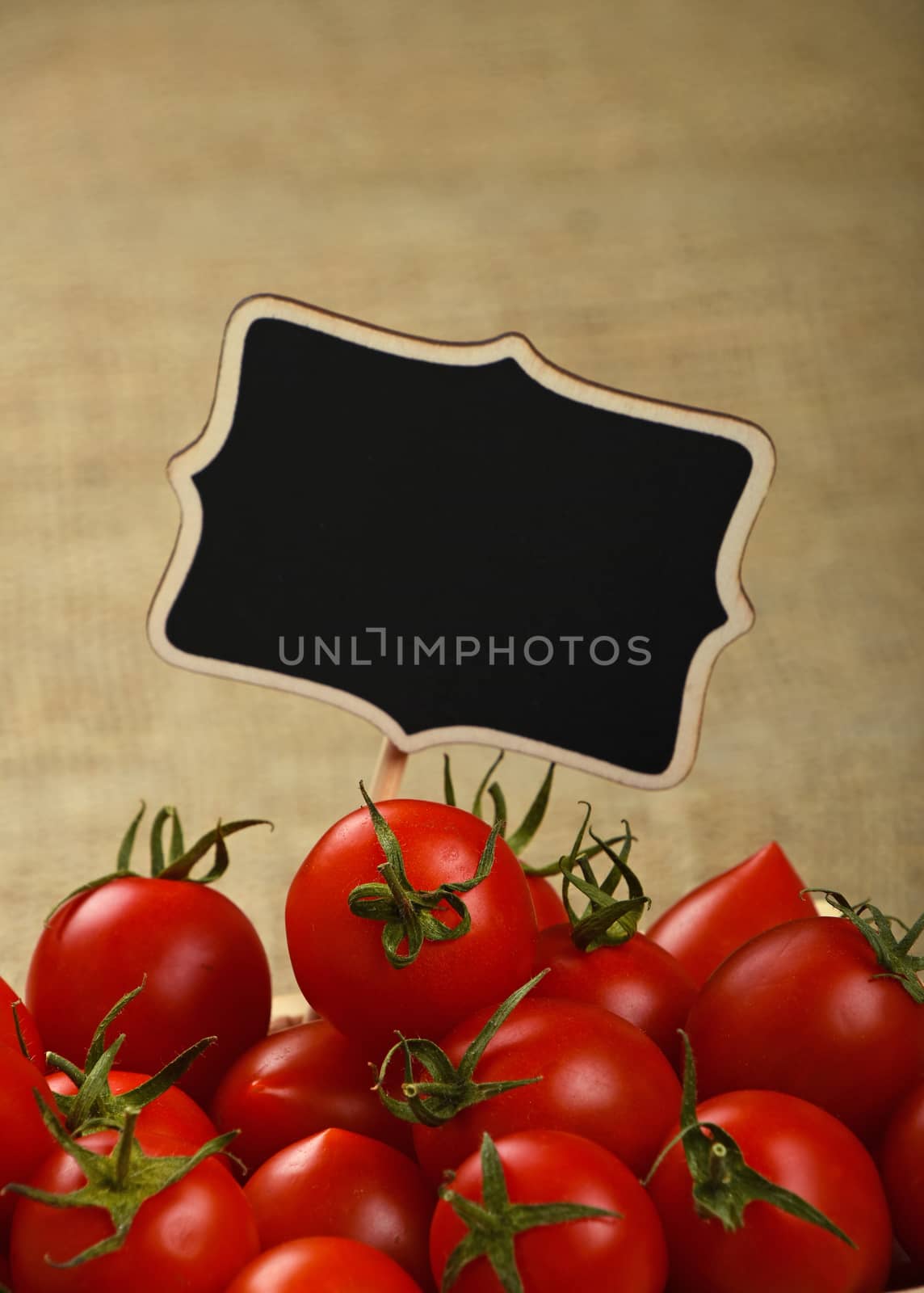 Red ripe fresh small cherry tomatoes with black wooden chalkboard price sign tag close up over jute burlap canvas background