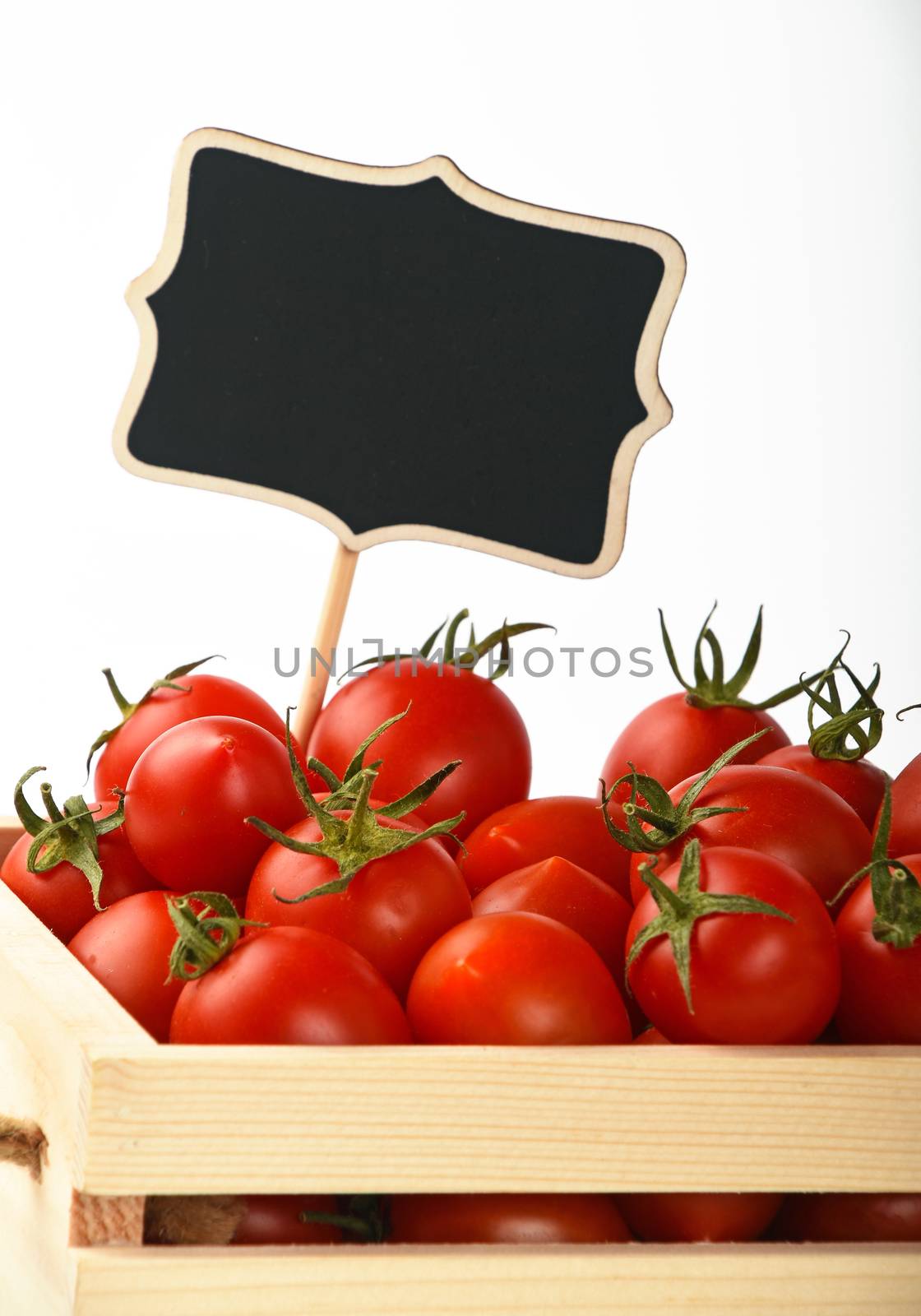 Fresh red ripe cherry tomatoes in small wooden box with black chalkboard price sign tag over white background