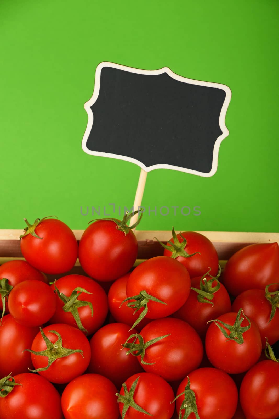 Fresh red ripe cherry tomatoes in small wooden box with black chalkboard price sign tag over green background, high angle view