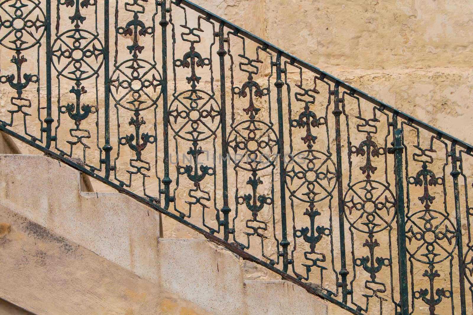 Part of the stairs from a side, with visible rhythm of the steps and iron handrail with motive of compass and anchor. Stone wall in the background. Island Malta