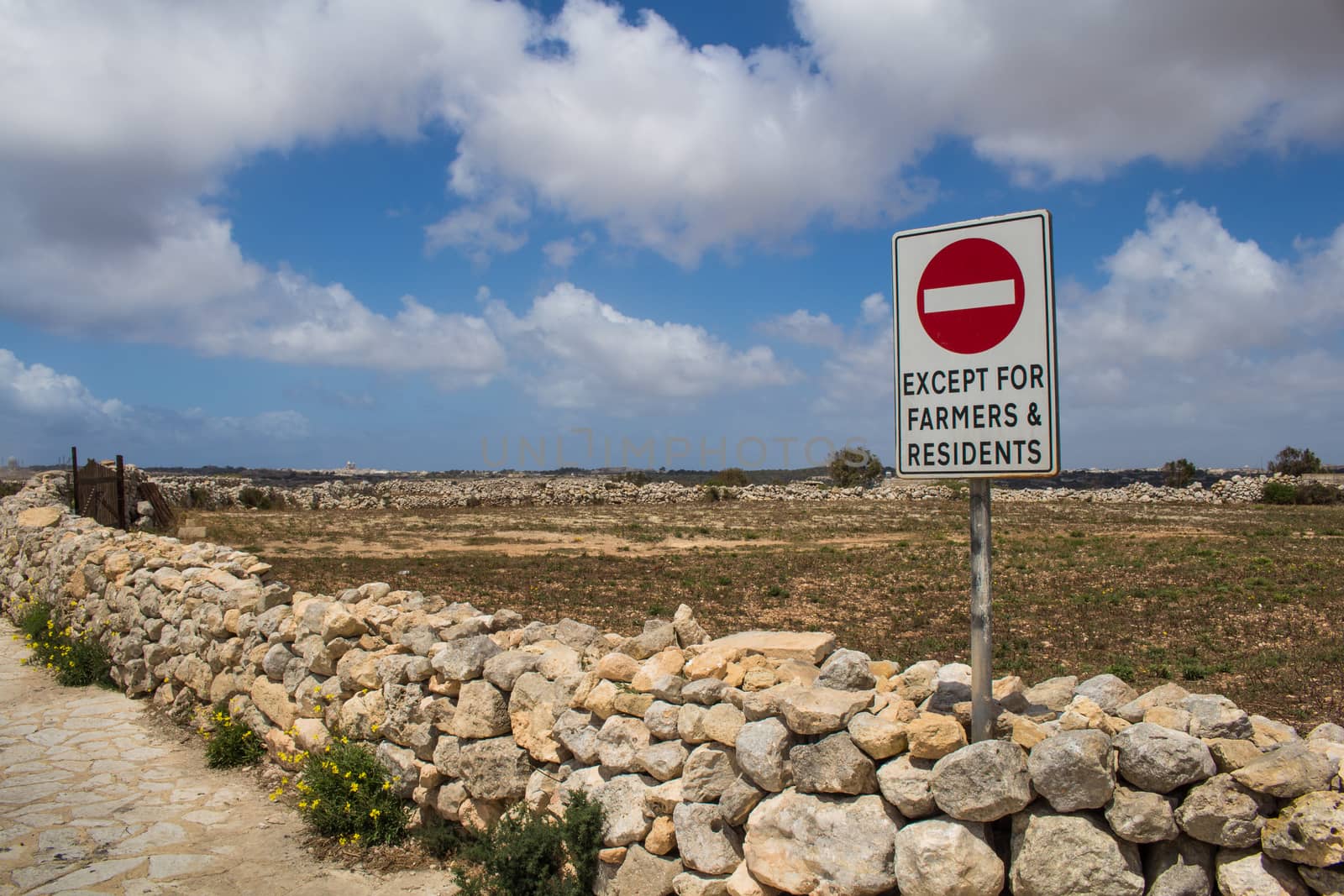 Fence made of stones lining a field. No entrance sign. Blue sky with intense white clouds. Mediterranean island Malta.