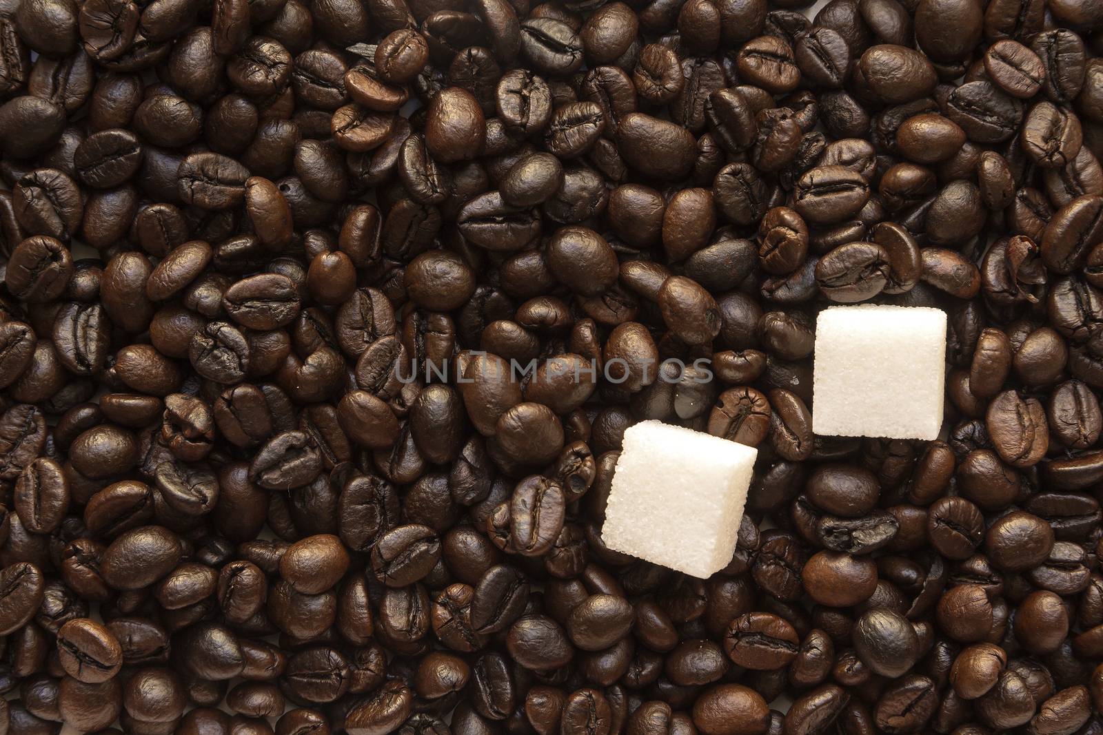 pieces of white sugar in coffee roasted beans Brown background