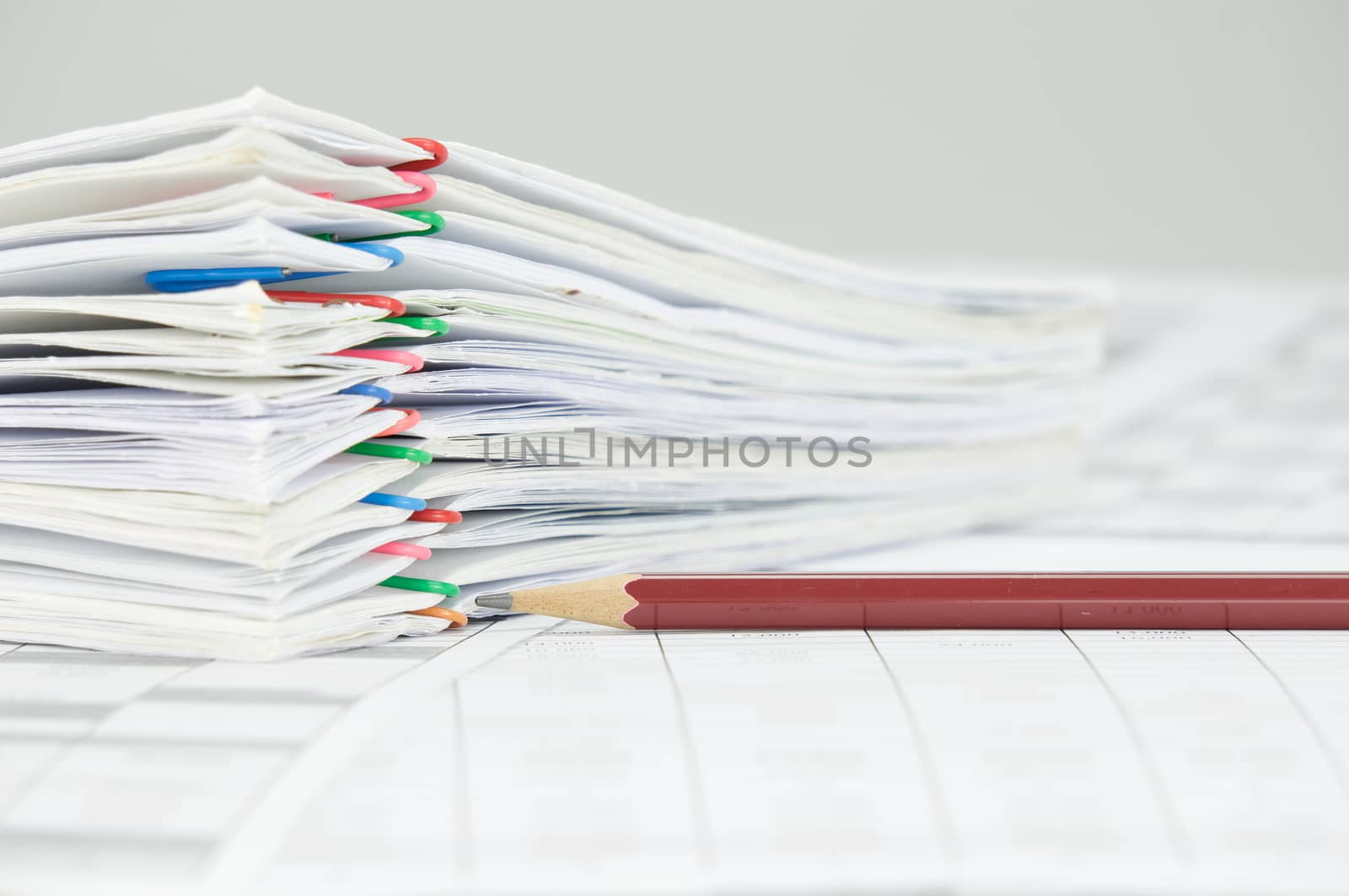 Brown pencil and overload of paperwork with colorful paperclip on finance account place on white background.