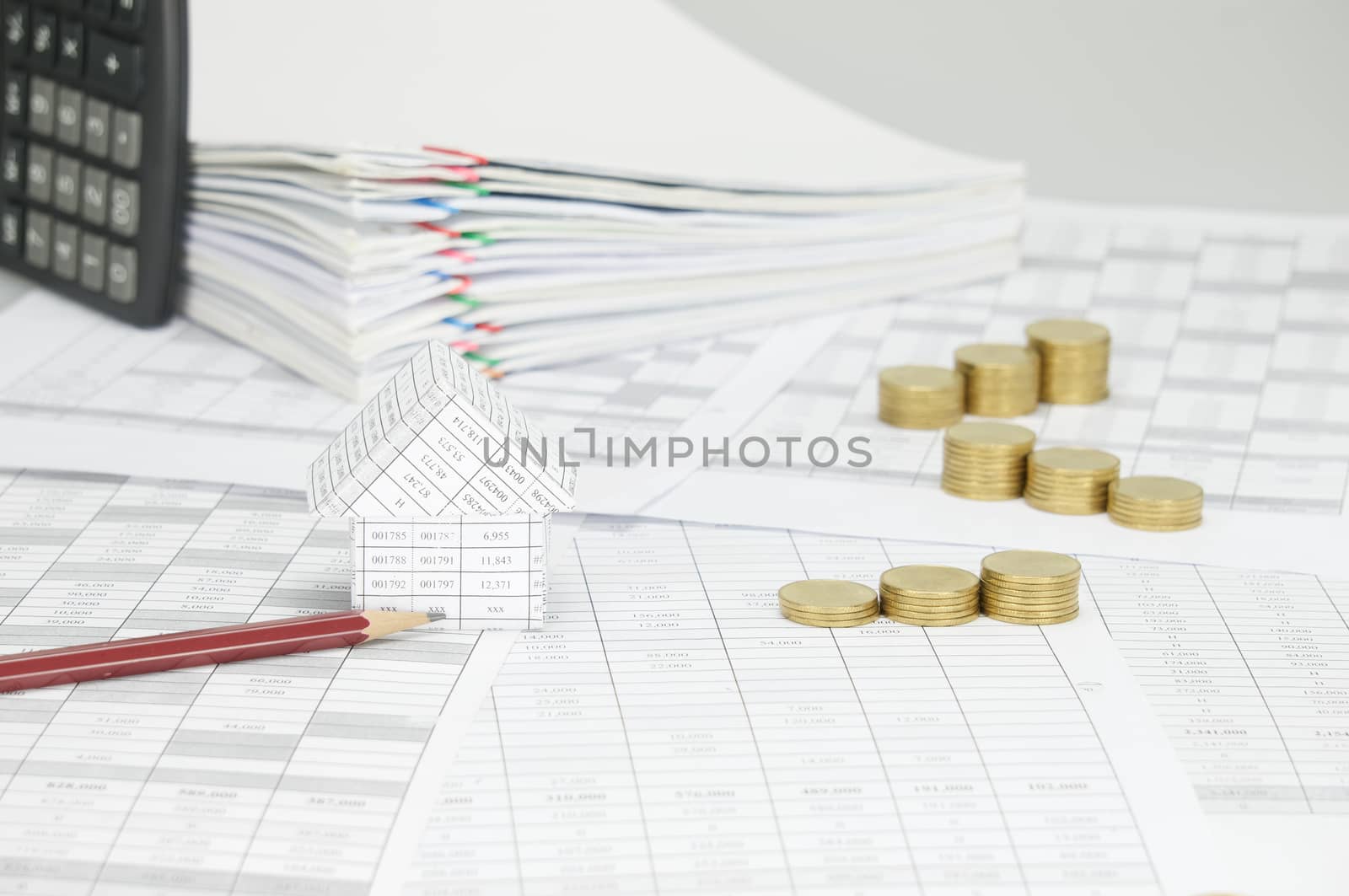 House with brown pencil and step pile of gold coins on finance account have blur calculator place vertical and overload of paperwork with colorful paperclip as background.