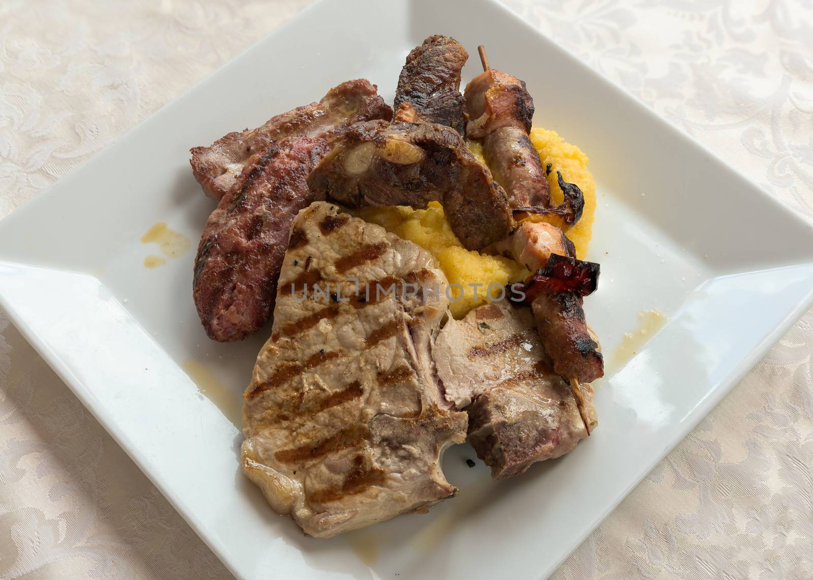 Typical italian grilled meat mix and Polenta on a plate at restaurant,from above.