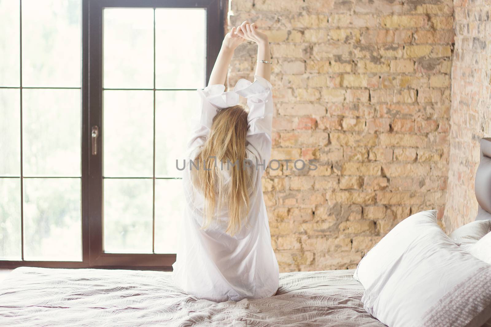 Woman stretching in bed after waking up, back view