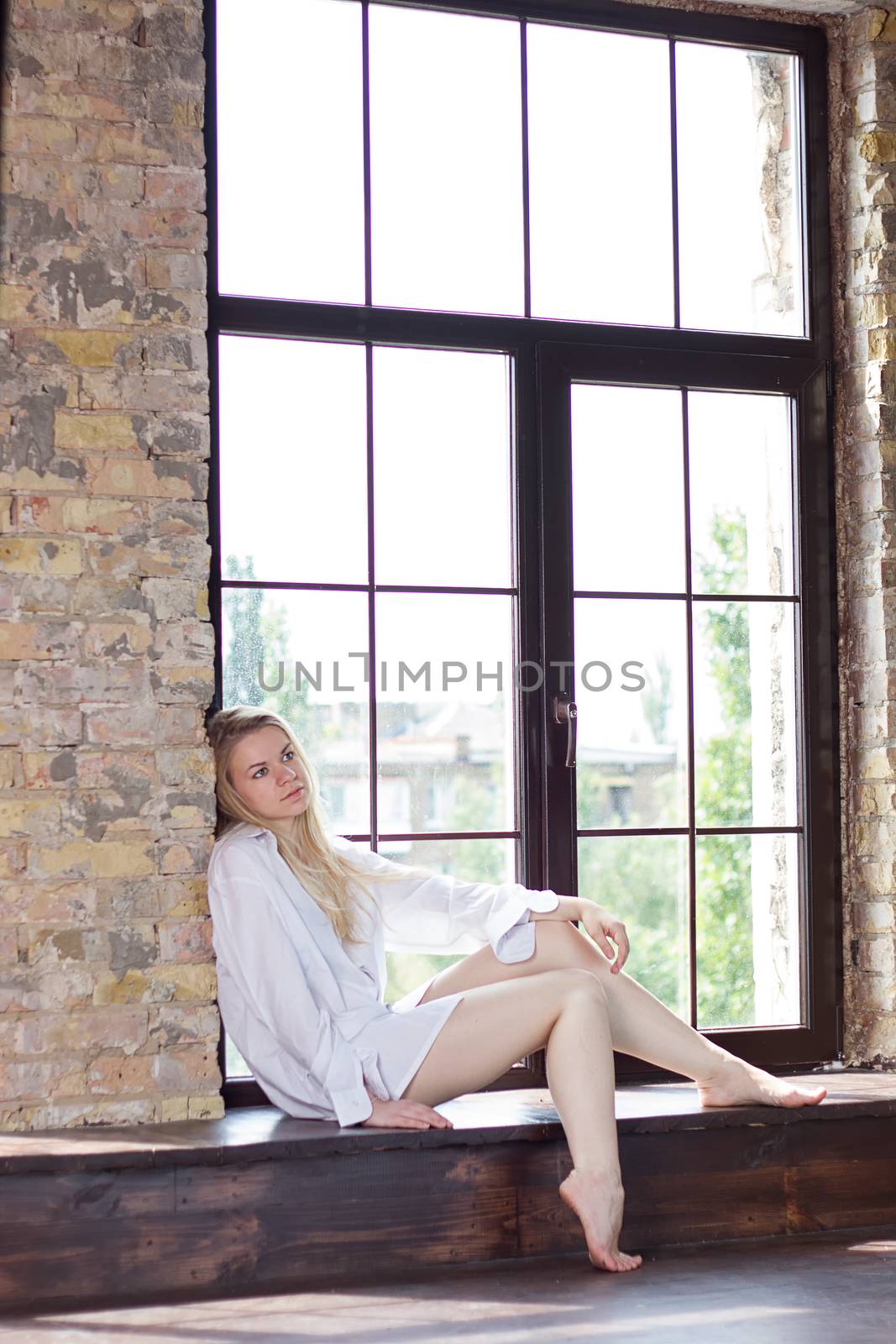 girl in a white men's shirt near a huge window