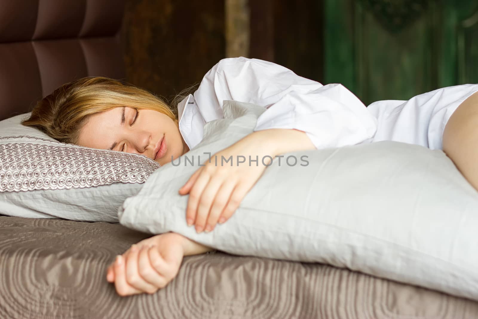 girl sleeps on the bed in a white men's shirt and hugging a pillow