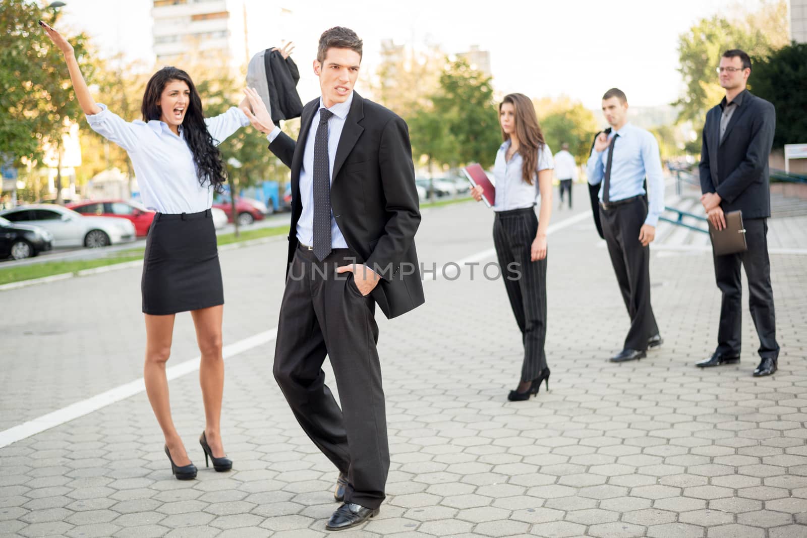 Young handsome businessman dressed elegantly indifferent waved his hand toward a young attractive businesswoman who yelling at him on the street in front of colleagues who viewed their fight.