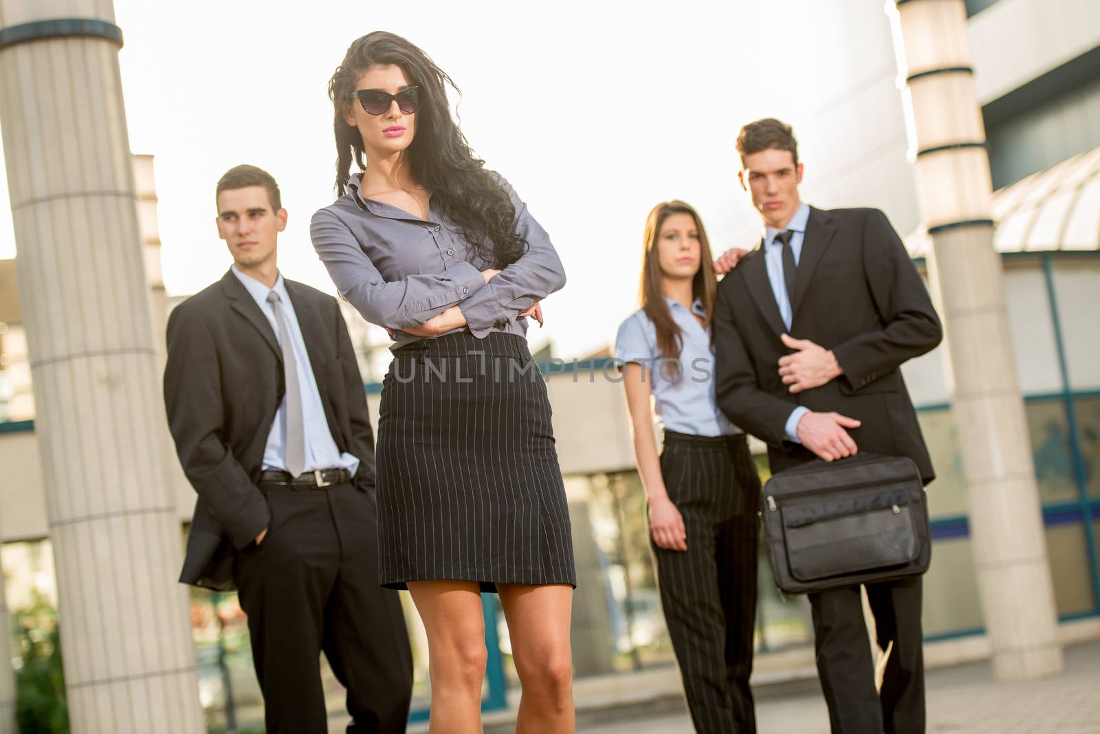 Young pretty and attractive businesswoman standing with his business team in front of his company, proud of their success, looking at camera through sunglasses.