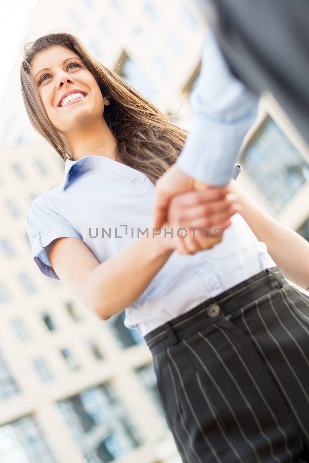 Young businesswoman elegantly dressed, which shake hands in front of a corporate building.