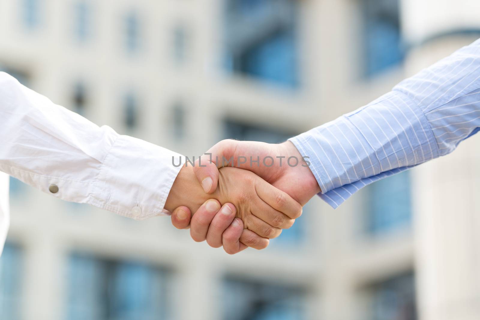 Hands of businessman and businesswoman shaking hands, while in the background looms office building.