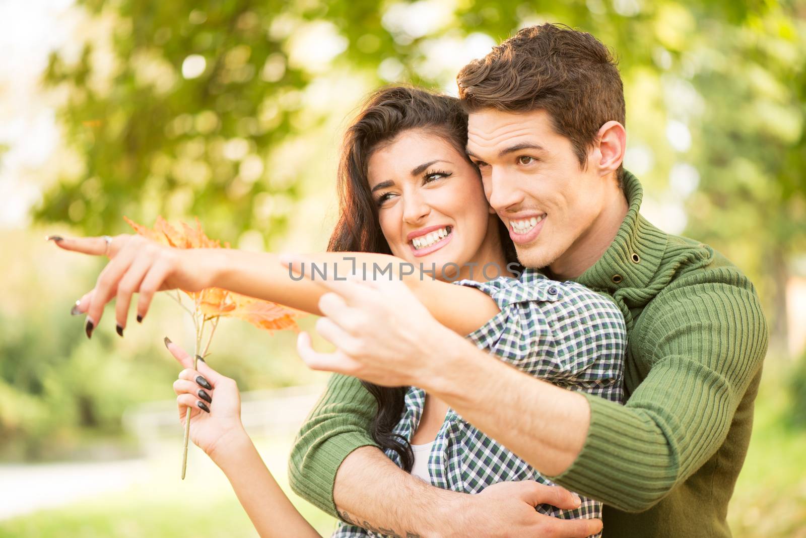 Young couple embrace in the park outstretched fingers of the hand pointing to something, while the girl carries in her hand a sprig of autumn leaves.