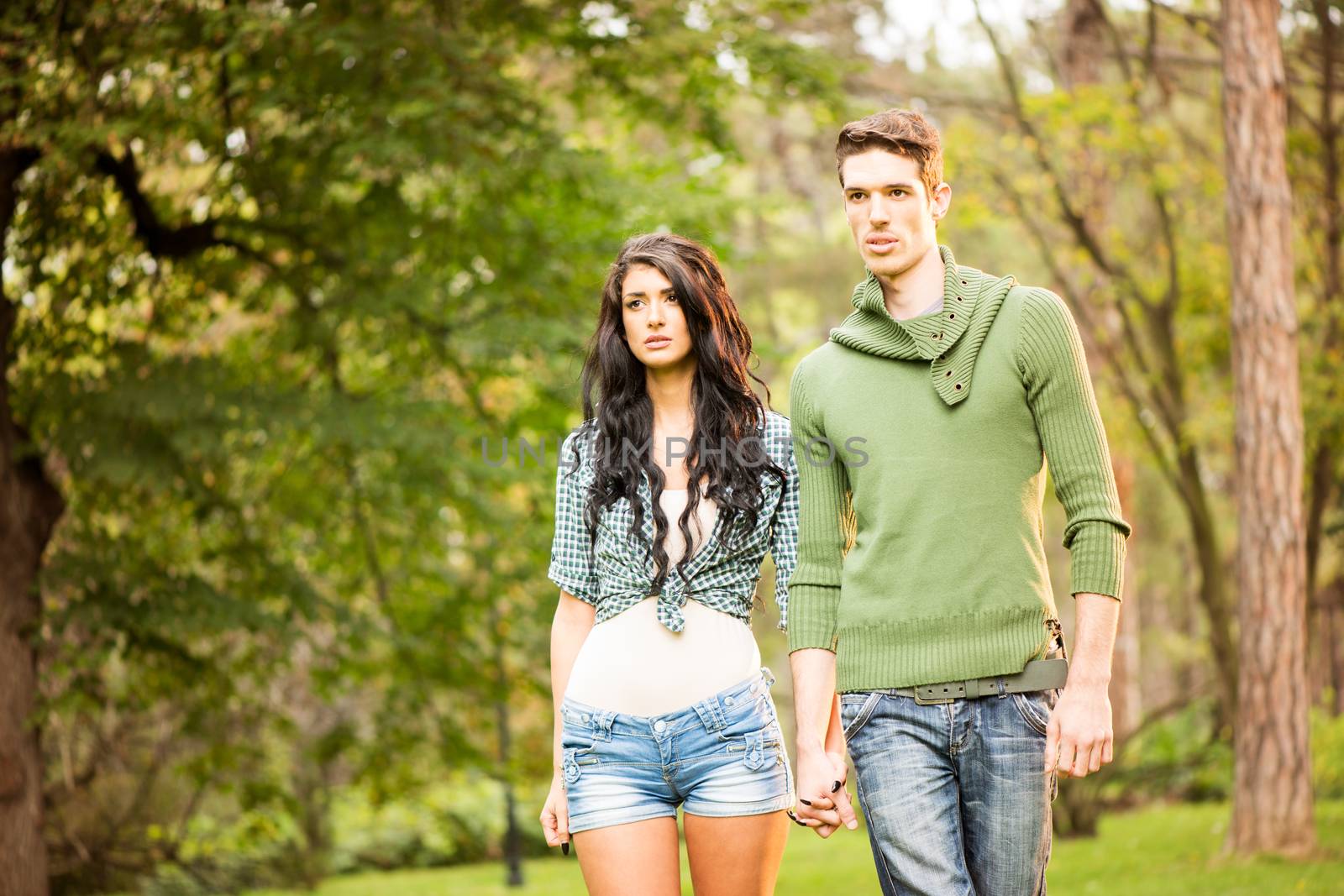 Young handsome heterosexual couple walking through the park holding hands.