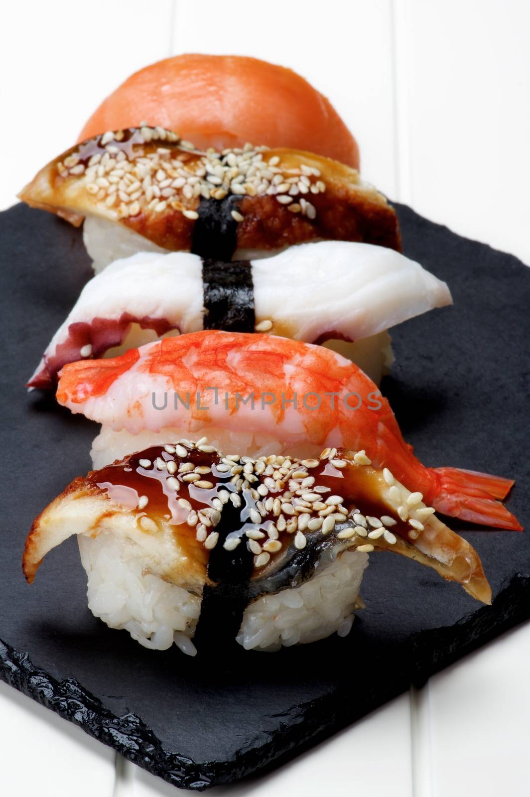 Various Sashimi Sushi with Smoked Eel, Shrimp, Octopus and Salmon In a Row on Stone Plate closeup on White Plank background. Focus on Foreground