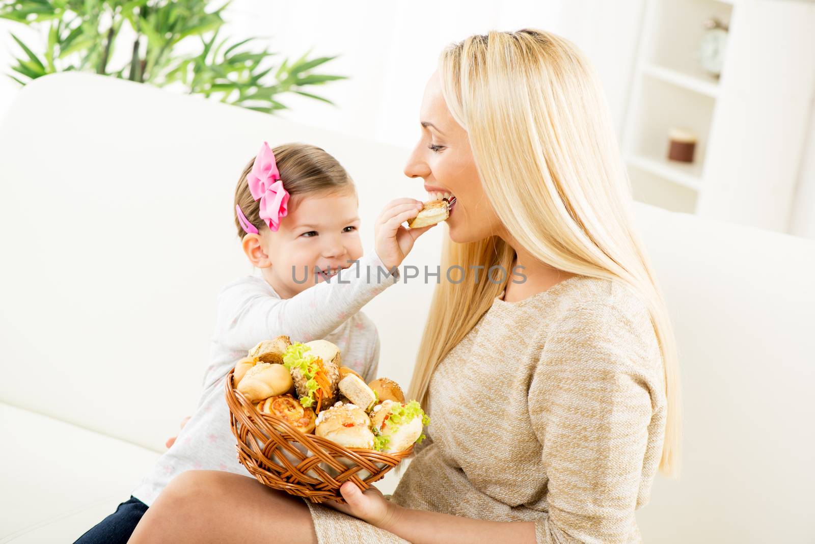 Cute little girl gives her beautiful mom snack of delicious pastry that she took from a basket held by her mother.