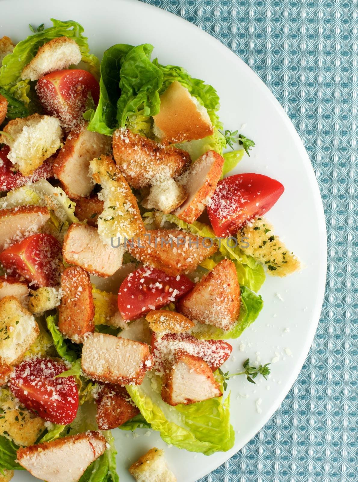 Half of White Plate with Delicious Caesar Salad with Roasted Chicken Breast, Garlic Crouton, Romaine Lettuce, Cherry Tomatoes and Grated Parmesan Cheese closeup on Blue Napkin