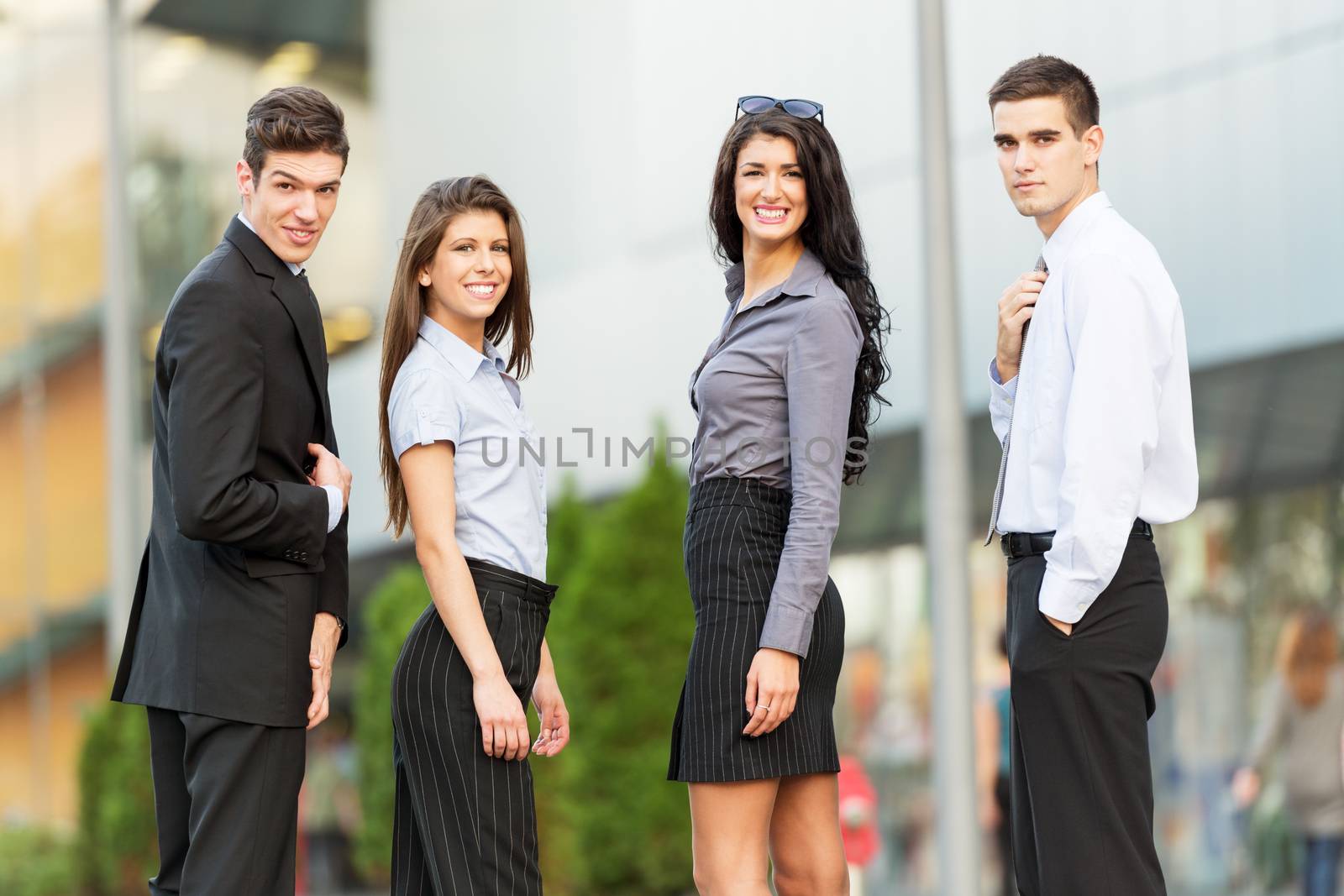 Portrait of group of young successful business people dressed in suits, standing in front of office building, smiling looking at camera.