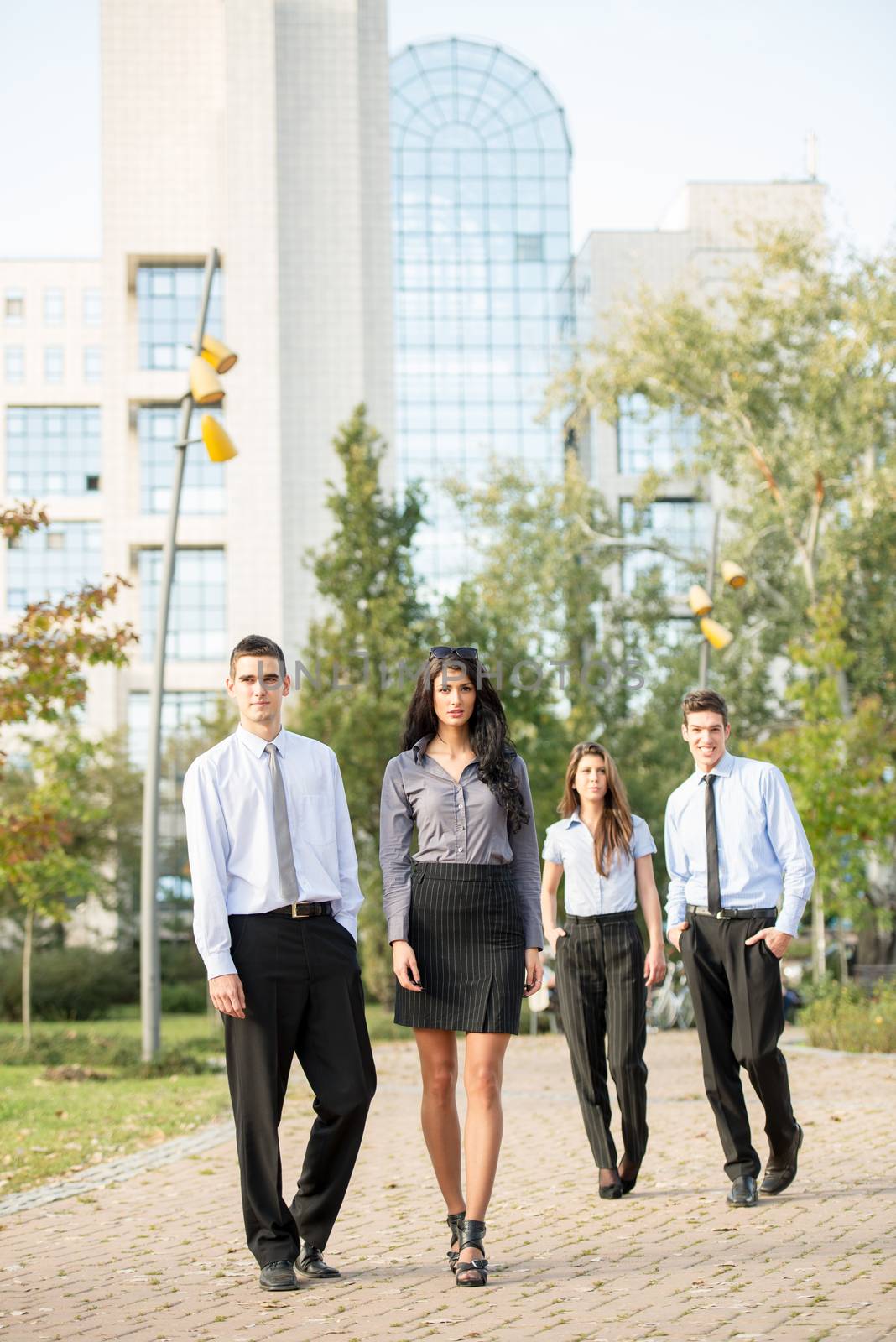 Group of young business people, formally dressed, walking through a park near their company.